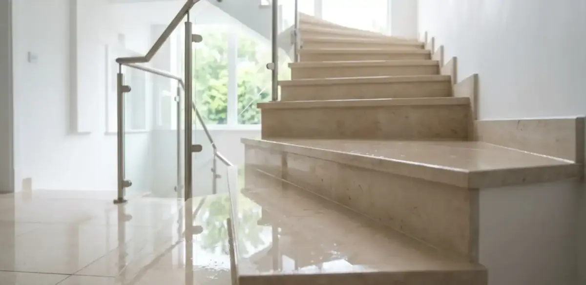 Helle Marmor-Treppe in einem Wohnhaus in Köln nach der wöchentlichen Reinigung: spiegelnd polierte Stufen, sauberes Glasgeländer mit Edelstahl-Pfosten, Tageslicht durch die Fenster.
