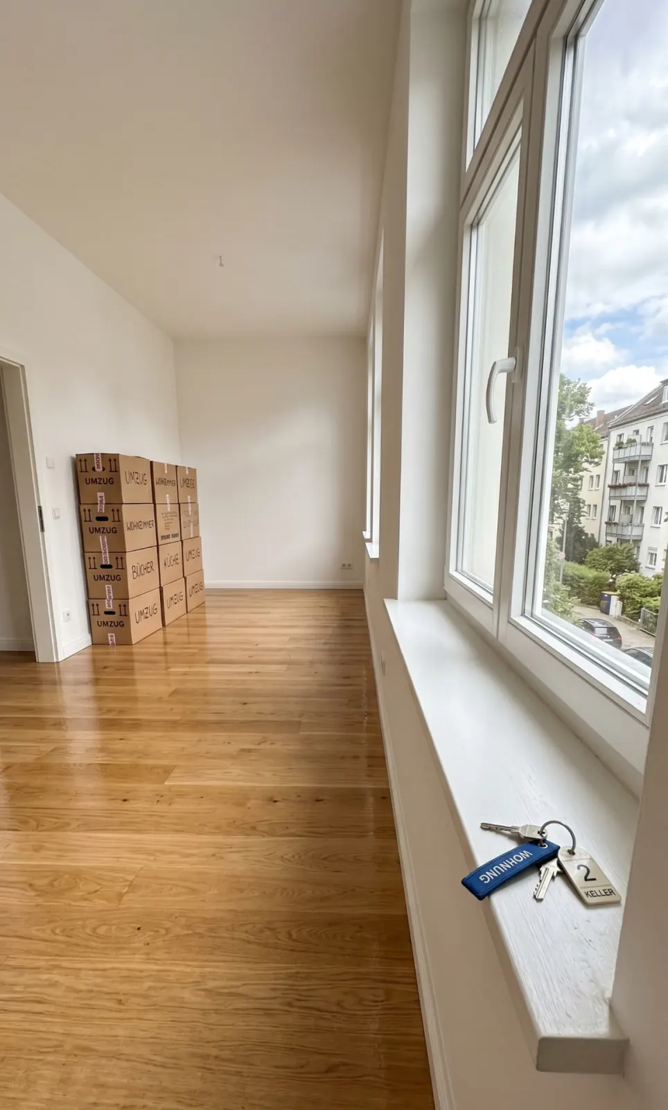 Leere Wohnung in Köln vor der Schlüsselübergabe: Umzugskartons in der Ecke, frisch gewischter Holzboden, Schlüsselbund auf der sauberen Fensterbank.